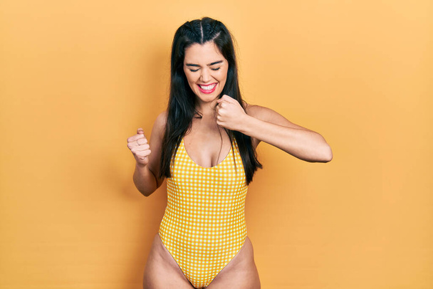 Young hispanic girl wearing swimsuit celebrating surprised and amazed for success with arms raised and eyes closed. winner concept.  - Photo, Image