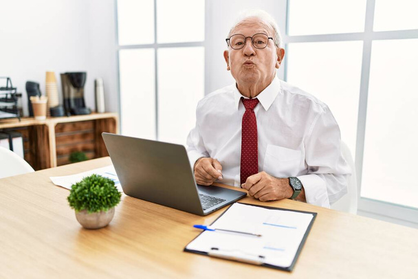 Старший чоловік працює в офісі, використовуючи комп'ютерний ноутбук, дивлячись на камеру, яка дме поцілунок в ефірі, мило і сексуально. вираз любові
.  - Фото, зображення