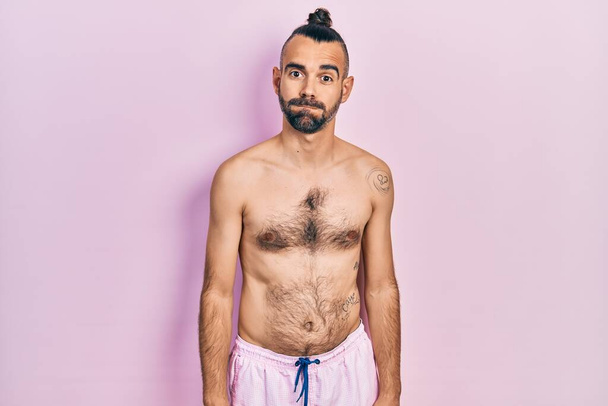 Jeune homme hispanique torse nu portant un maillot de bain gonflant les joues avec un visage drôle. bouche gonflée d'air, expression folle.  - Photo, image