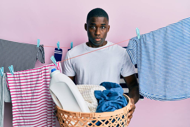 Jovem afro-americano segurando lavanderia cesta expressão indolor e confuso. conceito de dúvida.  - Foto, Imagem