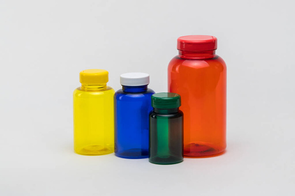 白い背景に複数の色の透明なプラスチック製の丸薬瓶。隔離。 - 写真・画像