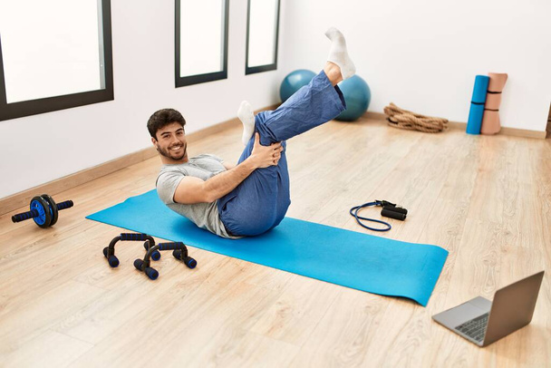 Junger hispanischer, sportlicher Mann lächelt glücklich beim Online-Sportkurs im Fitnessstudio. - Foto, Bild