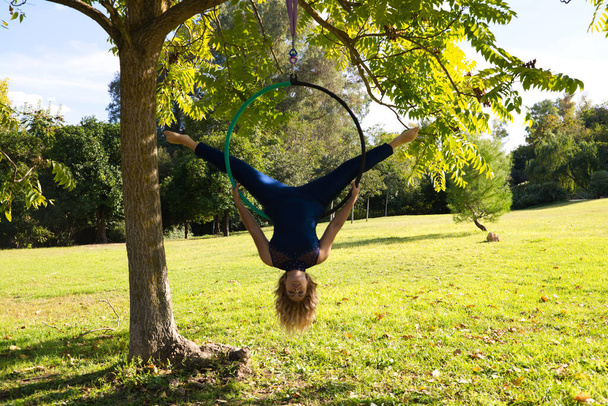Blondine vrouw en jonge turner acrobaat atleet uitvoeren van antenne-oefening op de lucht ring buiten in het park. Lithe vrouw in blauw kostuum voert poses van circus performers dansen met heupen. - Foto, afbeelding
