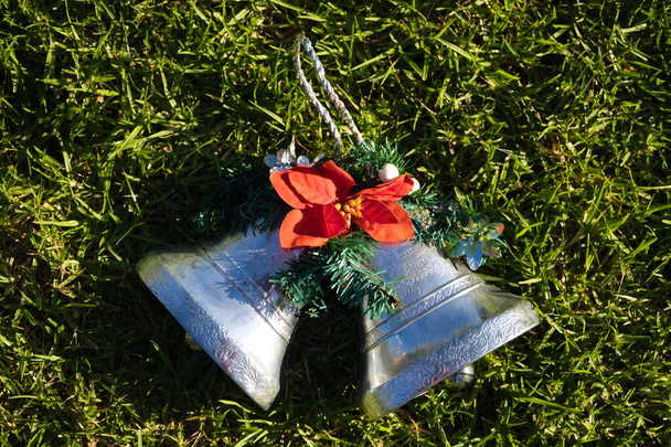 Ozdoba świąteczna, dwa srebrne dzwony z poinsetcją na trawniku ogrodu. Wesołych Świąt koncepcja - Zdjęcie, obraz