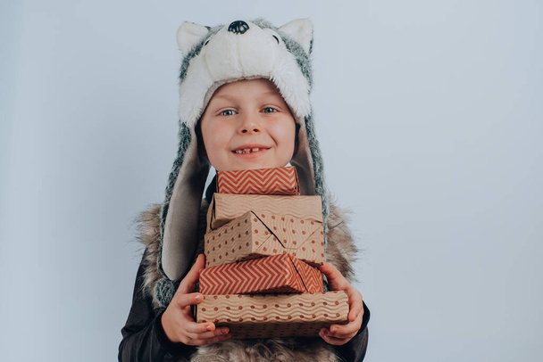 Egy fiú farkasjelmezben karácsonyi ajándékkal, szürke alapon elszigetelt kézműves papírba csomagolva. Nulla hulladék, műanyagmentes. - Fotó, kép