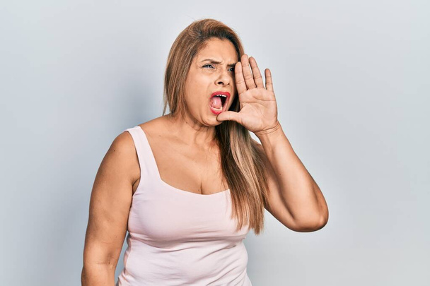 Middle age hispanic woman wearing casual style with sleeveless shirt shouting and screaming loud to side with hand on mouth. communication concept.  - Photo, Image