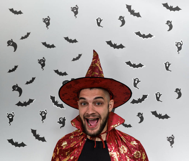 Bannière minimaliste célébrant Halloween avec homme caucasien barbu en costume de sorcière et fantômes noirs et chauves-souris sur fond blanc. Joyeux chapeau de magiciens ou sorciers. - Photo, image