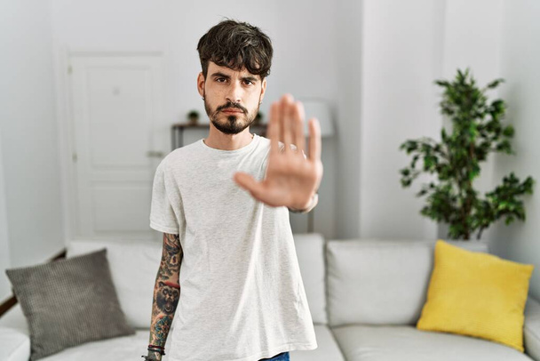 Hispanic man with beard at the living room at home doing stop sing with palm of the hand. warning expression with negative and serious gesture on the face.  - Foto, Bild