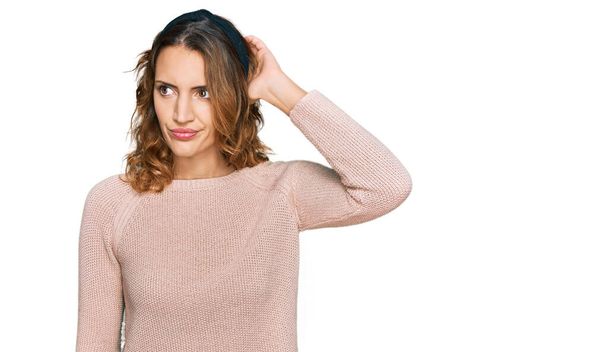 Beautiful young caucasian woman wearing casual sweater confuse and wondering about question. uncertain with doubt, thinking with hand on head. pensive concept.  - Photo, Image
