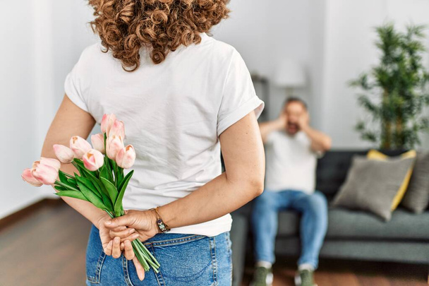 Kobieta zaskakująca męża kwiatami w domu. - Zdjęcie, obraz