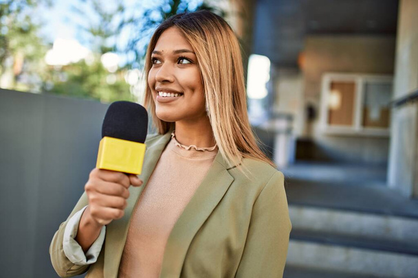 Jovem latina sorrindo confiante usando microfone na rua - Foto, Imagem