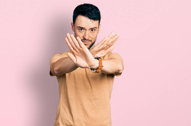 Hombre hispano con barba con expresión de rechazo casual camiseta cruzando brazos y palmas haciendo signo negativo, cara enojada  - Foto, Imagen