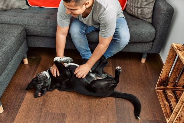 Jeune homme hispanique souriant heureux de jouer avec le chien à la maison. - Photo, image