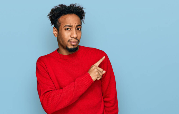 Young african american man with beard wearing casual winter sweater pointing aside worried and nervous with forefinger, concerned and surprised expression  - Photo, Image