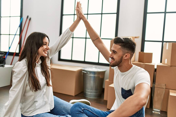 Joven pareja hispana haciendo símbolo de la casa con los brazos levantados en casa nueva. - Foto, Imagen