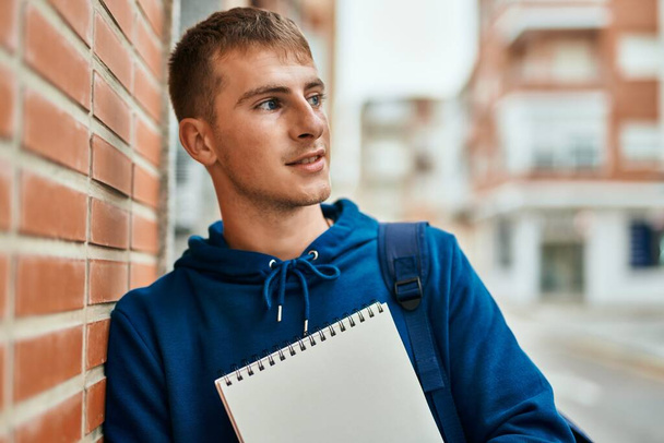 jong blond student glimlachen gelukkig vasthouden notebook op de universiteit. - Foto, afbeelding