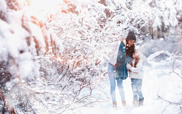 Νεαρή οικογένεια για μια βόλτα. Η μαμά και η κόρη περπατούν σε ένα χιονισμένο πάρκο.. - Φωτογραφία, εικόνα