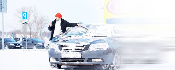 Egy férfi sofőr áll egy autó előtt. A tulajdonos télen takarítja az autót a hótól. Autó hóesés után. - Fotó, kép