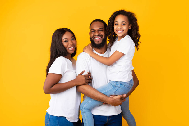 gelukkig zwart man poseren met vrouw en glimlachen schattig dochter - Foto, afbeelding