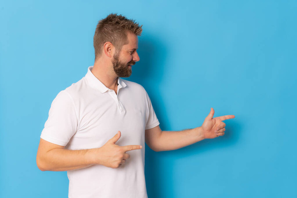Portrait of a happy bearded man pointing fingers up at copy space isolated over blue background - Foto, immagini
