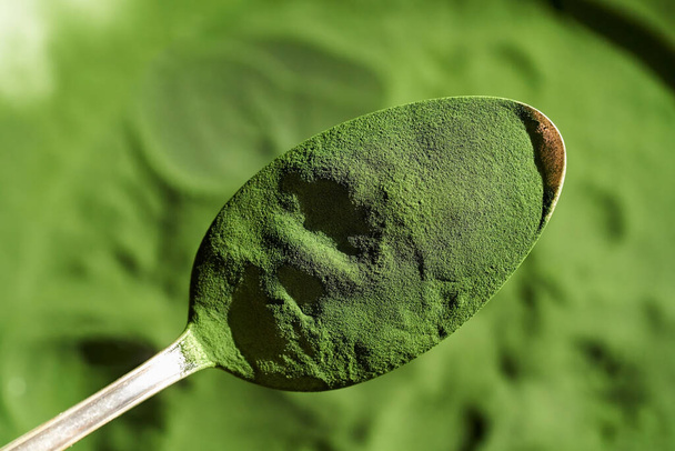 Green chlorella algae powder on a spoon, close up - Foto, afbeelding