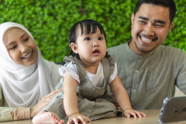 Сімейна мить: молода пара малайя з малюком у ресторані посміхається один одному
 - Фото, зображення