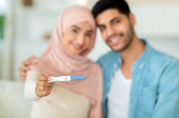 Müslüman kadın ellerinin kocasına sarılması ve kameraya gülümsemesi pozitif gebelik testine yakındır. - Fotoğraf, Görsel