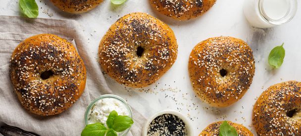 Variety fresh whole-grain bagels with poppy seeds, sesame seeds and ingredients for breakfast on a light concrete or stone background. Selective focus. Top view. Copy space. - Photo, Image