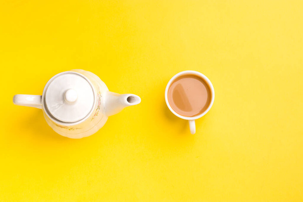 Tè al latte su tazza bianca con bollitore bianco su sfondo giallo immagine stock. - Foto, immagini