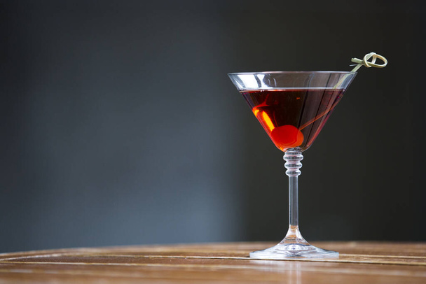 Zbliżenie kieliszka czerwonego koktajlu alkoholowego z wisienką na drewnianej beczce - Zdjęcie, obraz