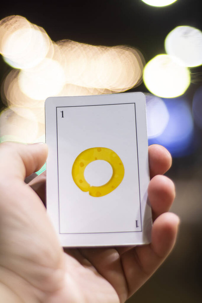 A vertical closeup of a human holding a game card with a yellow sign with a blurry background - Fotoğraf, Görsel