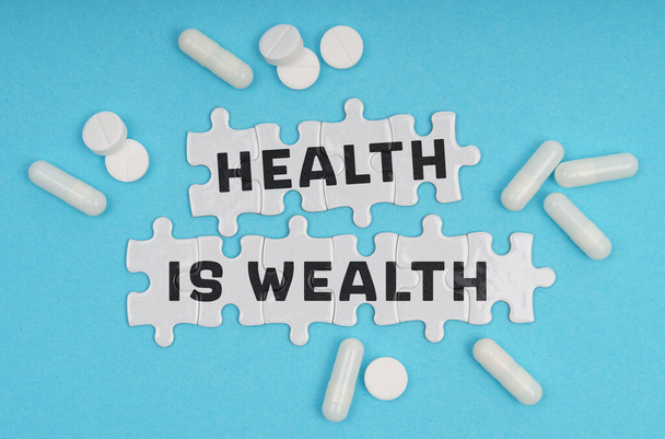 Medicine concept. On a blue background pills and puzzles with the inscription - Health Is Wealth - Fotoğraf, Görsel