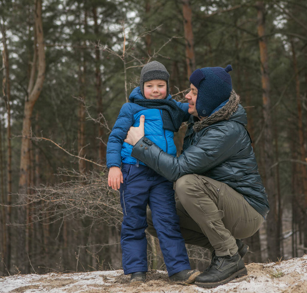 Happy family on a walk outdoors in sunny winter forest, Christmas holidays, father and son play together - Fotó, kép