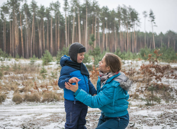 Happy family on a walk outdoors in sunny winter forest, Christmas holidays, mather and son play together - Foto, imagen
