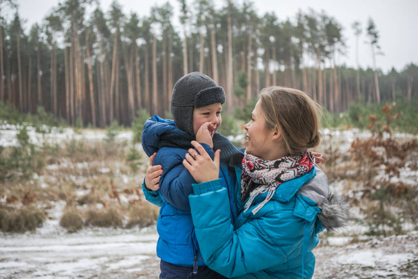 Famiglia felice in una passeggiata all'aperto nella soleggiata foresta invernale, vacanze di Natale, mather e figlio giocano insieme - Foto, immagini