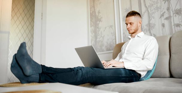 un jeune homme travaille sur un ordinateur portable sur le canapé à la maison. Photo de haute qualité - Photo, image