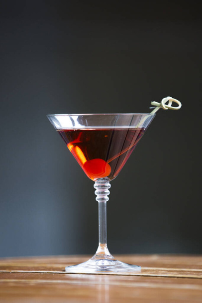 A vertical shot of a glass of red alcohol cocktail with a cherry on a wooden barrel - Fotografie, Obrázek