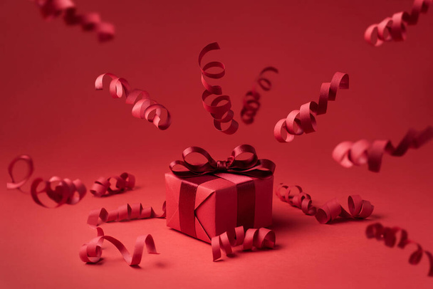Holiday and Christmas concept, gift and flying serpentine on a red background, festive background, close-up. - Photo, Image