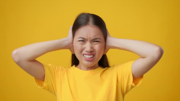 Donna asiatica che copre le orecchie con le mani scuotendo la testa, sfondo giallo - Filmati, video