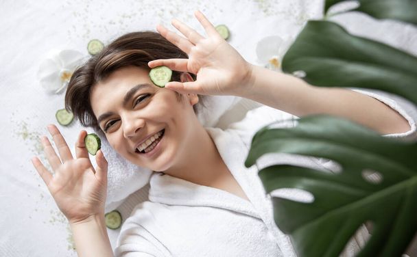 Happy young woman in a spa salon with cucumbers on her eyes, top view. - Photo, Image
