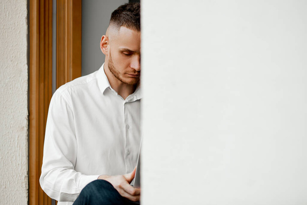 muž sedí doma na parapetu a dívá se na telefon - Fotografie, Obrázek
