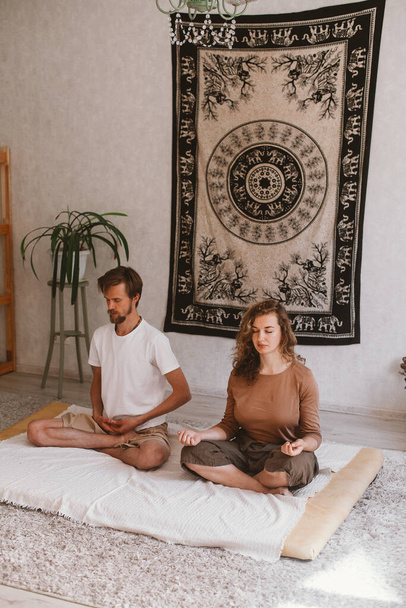 A vertical shot of a young couple practicing yoga and meditating at home - Fotoğraf, Görsel