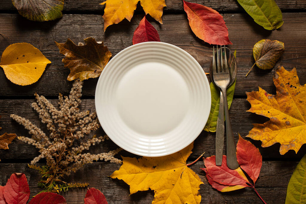 dinner plate stands on the table in autumn yellow-red leaves, autumn decor from the table, cutlery, table decorations - Photo, Image