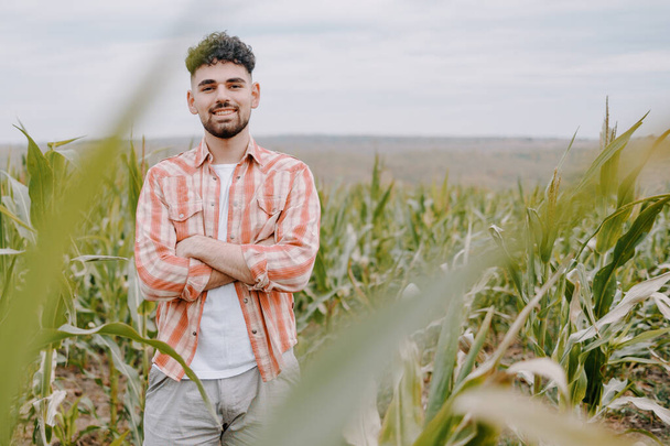 Portret młodego rolnika z skrzyżowanymi rękami. Przystojny młodzieniec na polu kukurydzy. Rolnictwo rolne i zbiory. - Zdjęcie, obraz