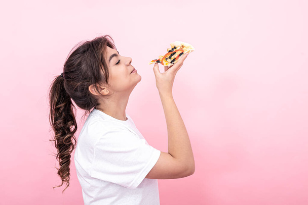 Atraktivní dívka s kusem pizzy na růžovém pozadí, kopírovací prostor. - Fotografie, Obrázek