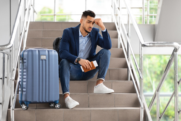 Upset Middle Eastern Guy Sitting On Airport Terminal Stairs With Luggage - Foto, Imagen