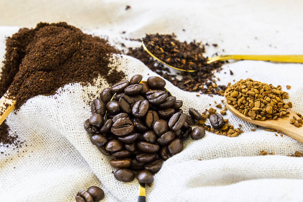 A closeup of roasted coffee beans and powder with wooden spoons on a white fabric - Photo, Image