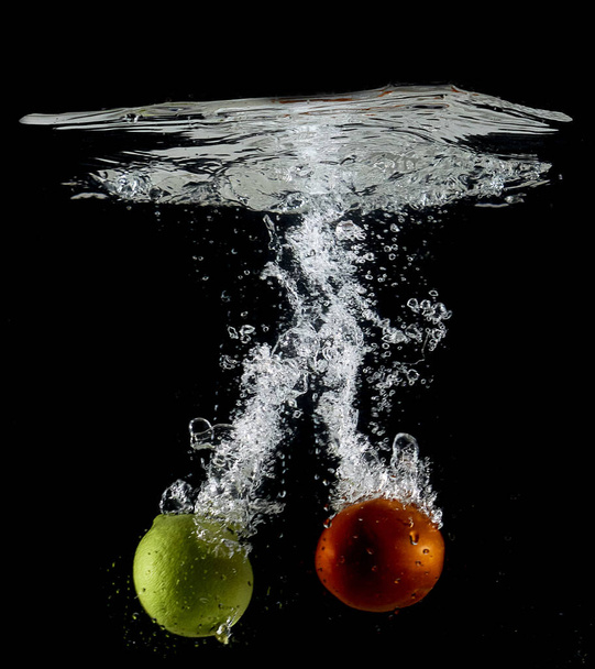 Fresh lemon and tomato immersed into the water in the black background - Foto, imagen
