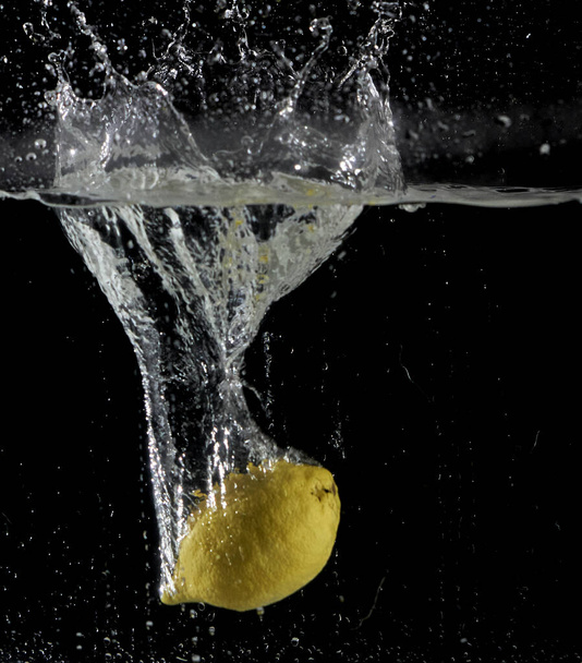 A fresh lemon dropped into water with a splash isolated in the black background - Photo, Image