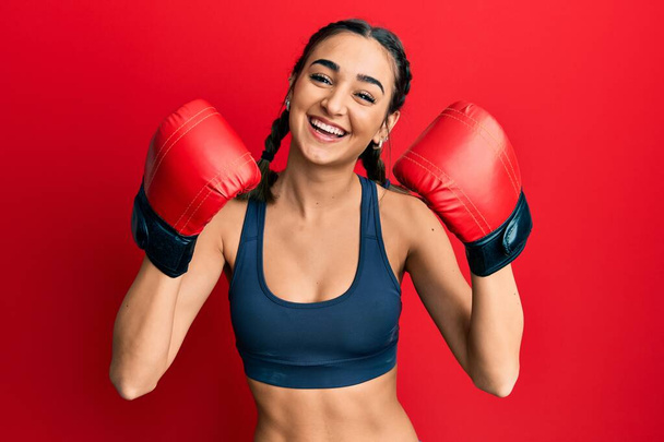 Young brunette girl using boxing gloves wearing braids smiling and laughing hard out loud because funny crazy joke.  - Foto, afbeelding